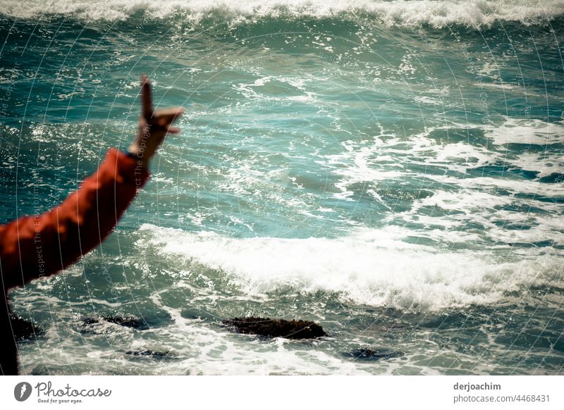 konstruktiv  / Die erhobe Hand mit dem roten Ärmel  steht am schäumenden Meer und warnt vor der nicht sichtbaren Unterströmmung die Schwimmer am Strand.