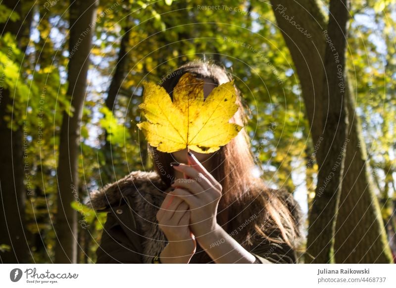 Frau mit Herbstblatt vorm Gesicht im Wald Natur Herbstlaub Außenaufnahme Junge Frau Herbstbeginn herbstlich Herbstfärbung Herbstwald Herbstwetter