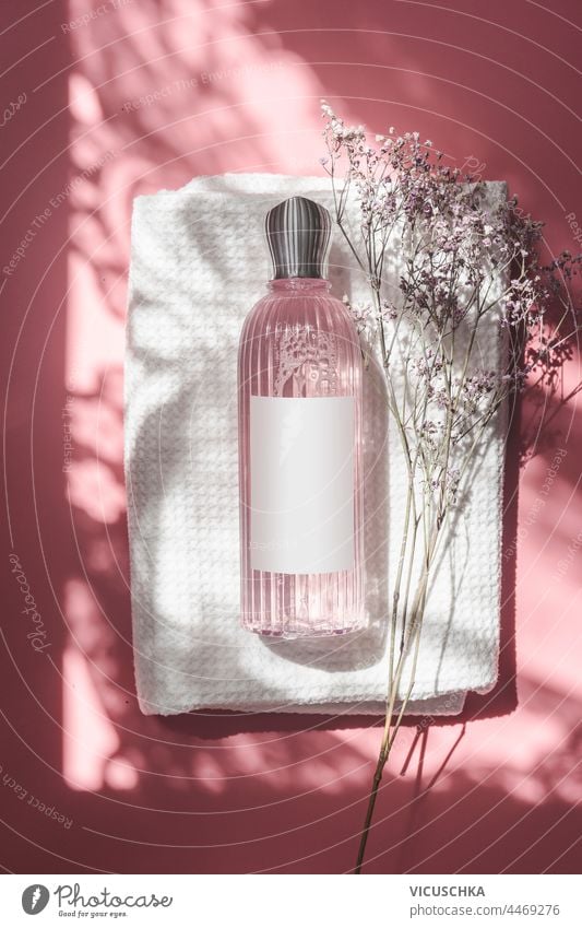 Rosa Kosmetikflasche mit leerem Etikett auf weißem Handtuch auf rosa Hintergrund im Sonnenlicht mit Ornament Schatten. Ansicht von oben Flasche blanko