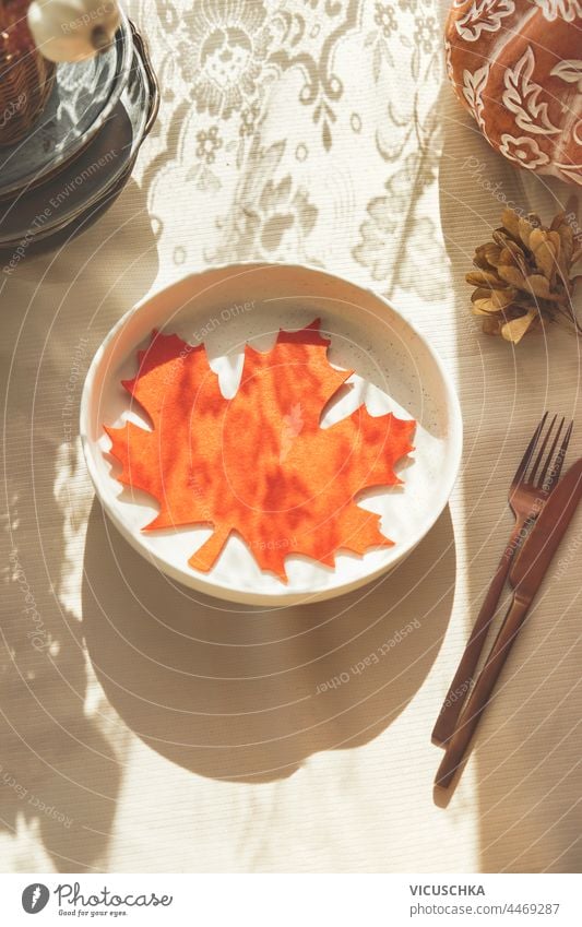 Orangefarbene Ahornblattdekoration auf einem Teller. Herbstlich gedeckter Tisch mit Sonnenlicht und Besteck. Ansicht von oben Dekoration & Verzierung