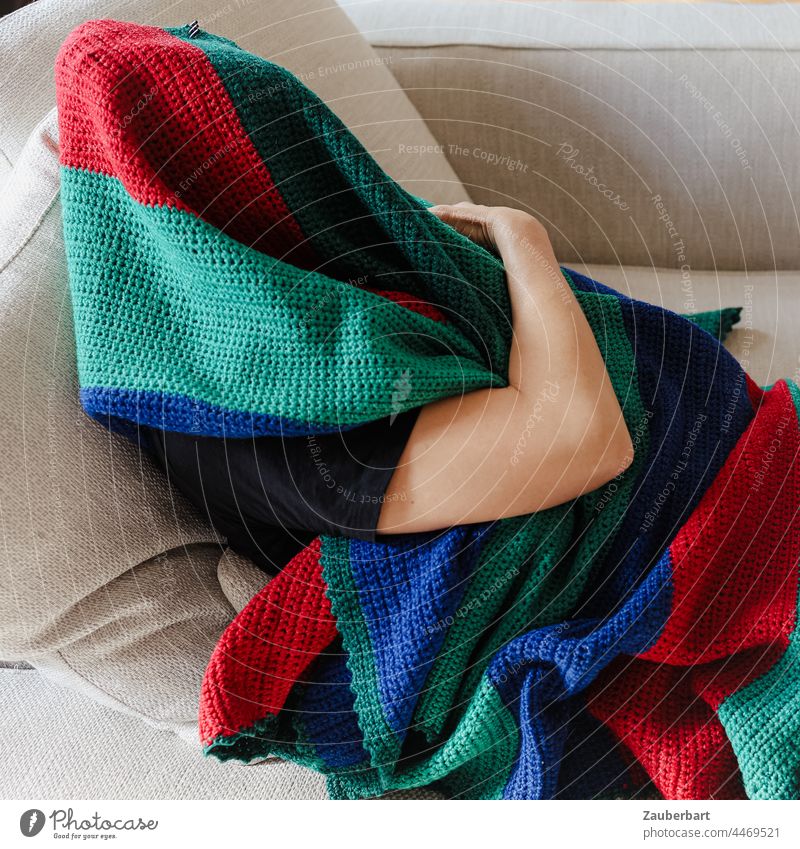 Mensch versteckt sich unter einer bunten Wolldecke auf dem Sofa Arm eingewickelt grün rot blau halten verstecken einwickeln Falten Textilien Stoff Schutz Decke
