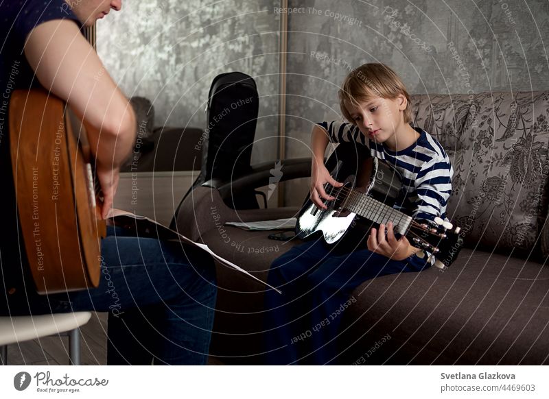 Junger männlicher Musiker bringt einem kleinen Jungen bei, wie man Akustikgitarre spielt und nach Noten spielt Lektion Gitarre Instrument Gitarrenspieler