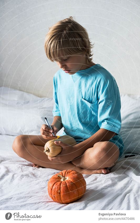 Blonde Junge macht Jack-o-Lantern zu Hause. Halloween DIY Konzept. Herstellung Kürbisse Dekor diy Farbe Filzstift Lifestyle fallen Kunst festlich Zeichnung Kind