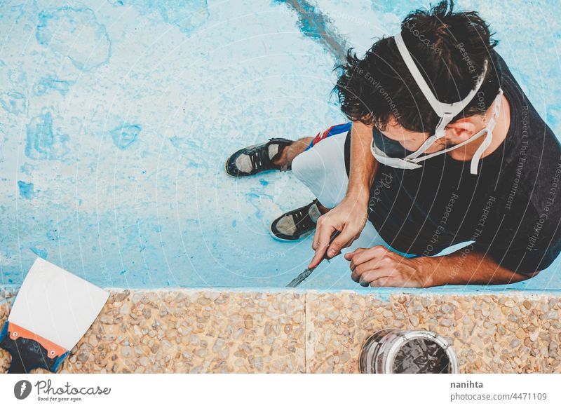 Junger Mann arbeitet in seinem Schwimmbad Flugzeugwartung diy Mundschutz Arbeit arbeiten Spachtelmasse Kittmesser Spachtelpalette Pool Schwimmsport blau türkis