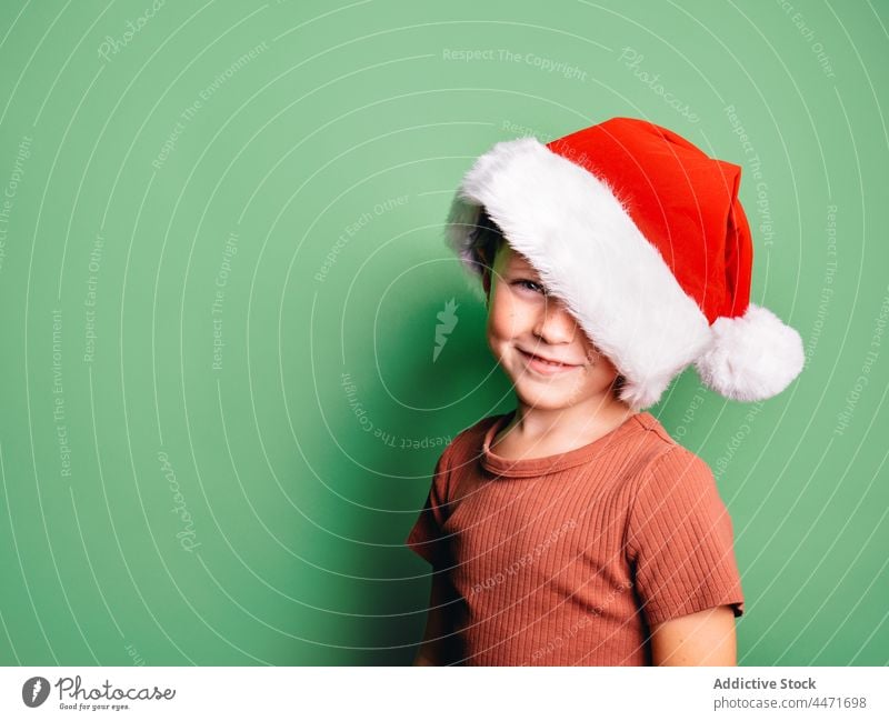 Lächelnder Junge mit Weihnachtsmannmütze im Studio stehend Kind Weihnachten Weihnachtsmütze Veranstaltung Feiertag feiern Anlass sorgenfrei positiv froh