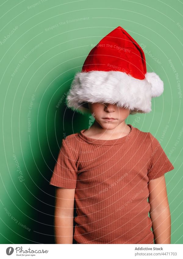 Anonymer Junge mit Weihnachtsmannmütze Weihnachten Feiertag Gesicht bedeckt Neujahr verärgert Tierhaut Veranstaltung Kind Dezember ernst Kindheit Vorabend