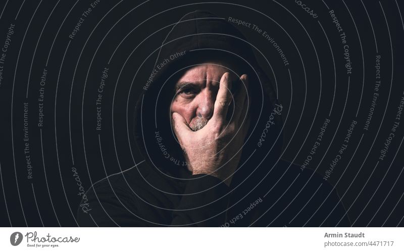 Porträt eines Mannes mit Kapuzenpulli, der eine Hand vor sein Gesicht hält Winkel Vollbart schwarz Unschärfe Atem lässig Kaukasier Nahaufnahme selbstbewusst