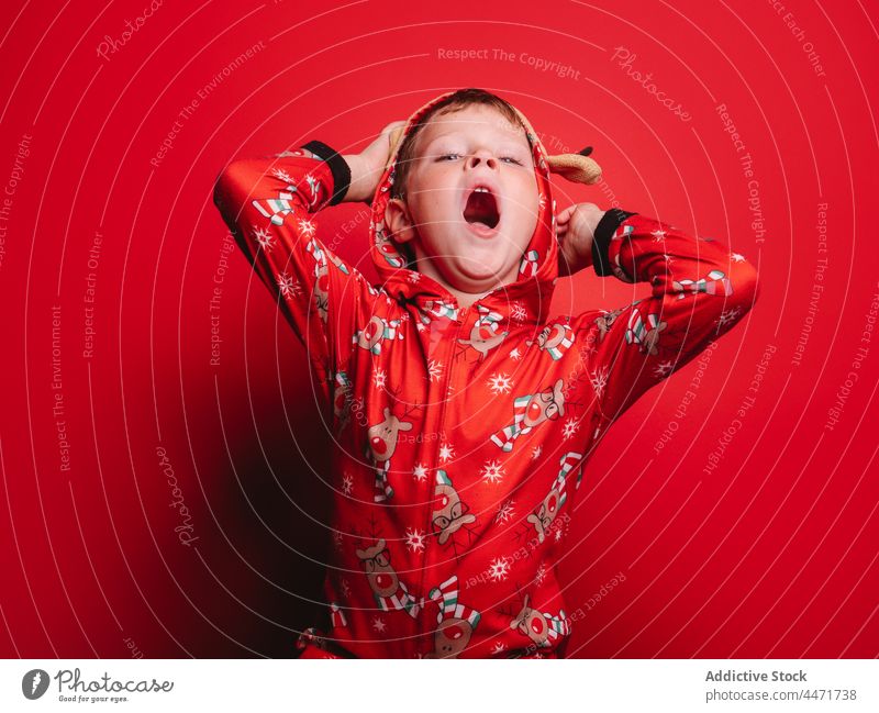 Niedliches Kind im Weihnachtskostüm gähnt im roten Studio gähnen Weihnachten schläfrig lustig Neujahr Porträt Junge Kindheit Dezember feiern Glück Pyjama