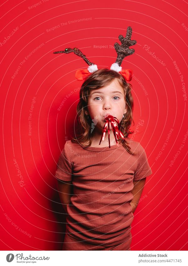 Glückliches Kind mit Gebläse in rotem Atelier während der Weihnachtsfeier Mädchen Party Weihnachten Freude feiern Feiertag positiv Porträt Hirsche Stirnband