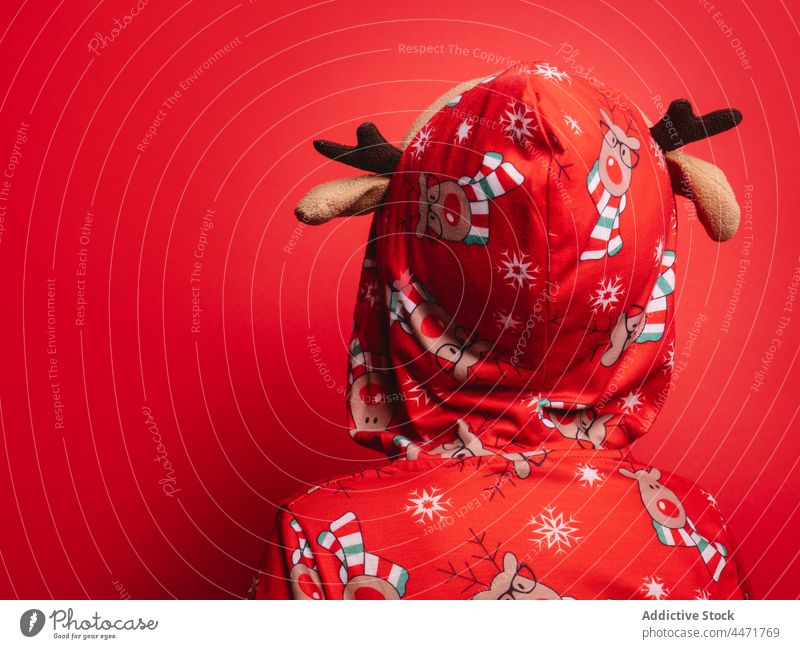 Anonymes Kind in rotem Studio während der Weihnachtsferien stehend Weihnachten Feiertag Pyjama lustig Kindheit feiern Winter Hirsche Kapuze Tradition unschuldig