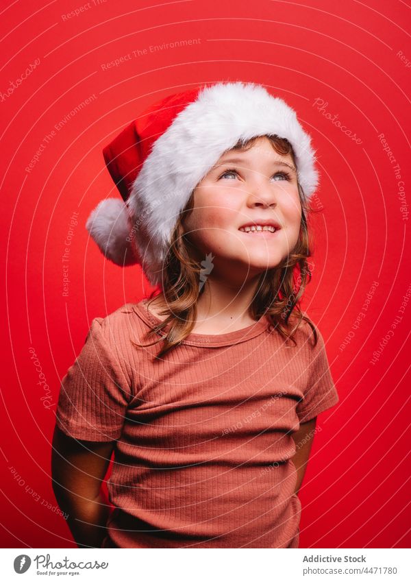 Fröhliches süßes Kind mit Weihnachtsmannmütze lächelnd in rotem Studio Weihnachtsmütze Weihnachten Mädchen Neujahr Lächeln Porträt Model Stil Tracht froh