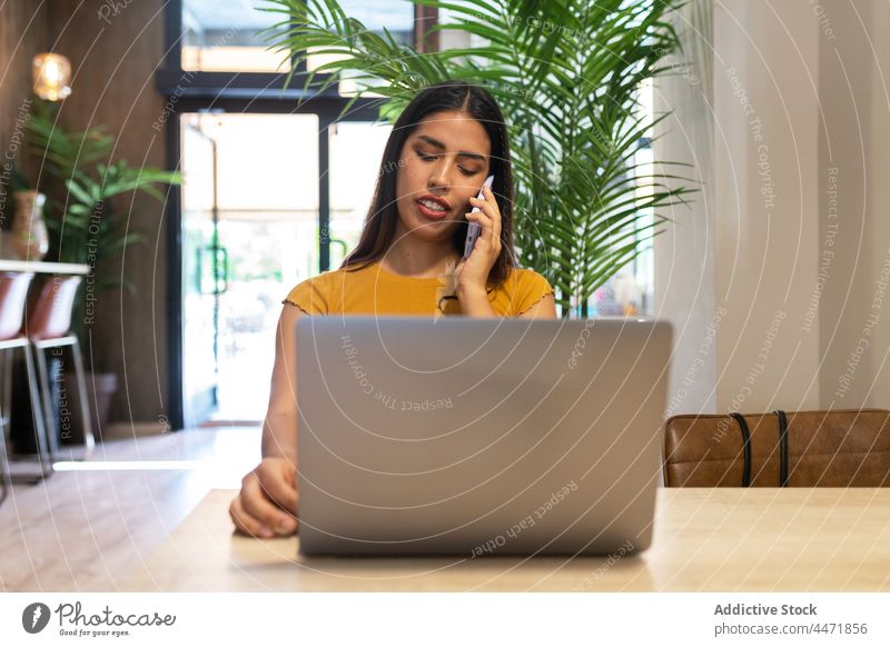Beschäftigte Frau, die mit ihrem Smartphone spricht und einen Laptop benutzt benutzend abgelegen Tippen Telefonanruf Arbeit zuschauen Projekt freiberuflich