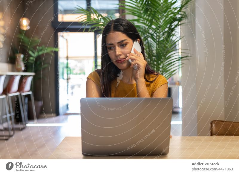 Beschäftigte Frau, die mit ihrem Smartphone spricht und einen Laptop benutzt benutzend abgelegen Tippen Telefonanruf Arbeit zuschauen Projekt freiberuflich