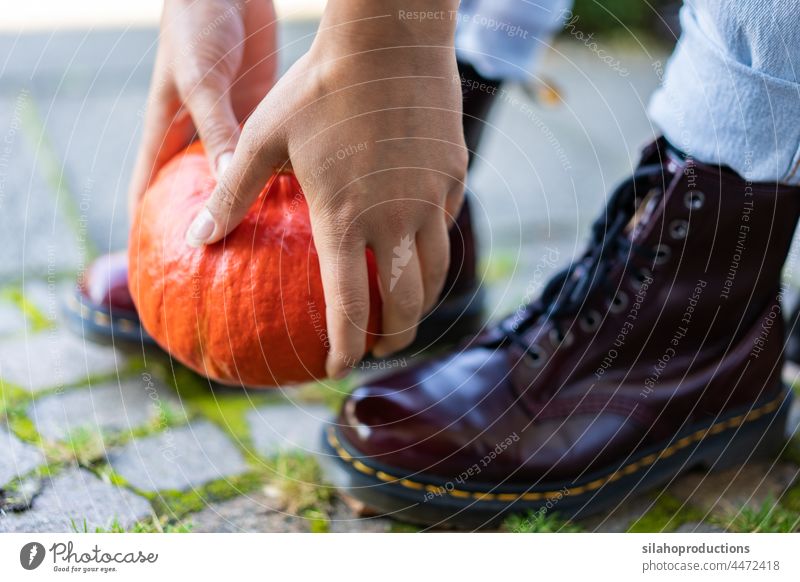 Nahaufnahme der Hände und Stiefel einer jungen Frau, die einen orangefarbenen Kürbis hochhebt. aktiv Erwachsener Herbst Hintergrund Körperteil Konzept Tag