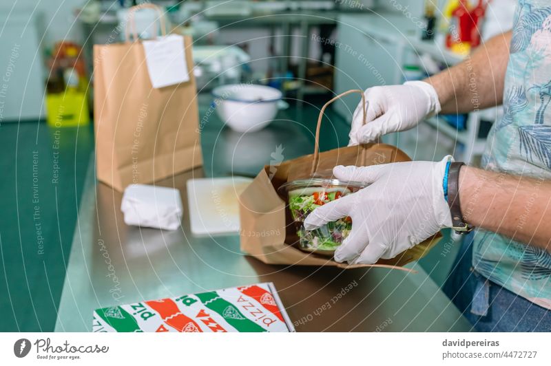 Unbekannter Koch beim Verpacken einer Bestellung zum Mitnehmen sichere Lebensmittel Verpackung Tüte Hauszustellung wegnehmen Bestellungen einpflanzend