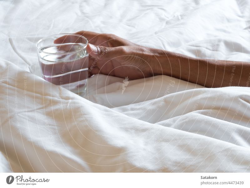 Die Hand hält das Glas Wasser auf dem Bett zerknittert Decke weiß weich Schlafzimmer trinken Hotel Schot Morgen unordentlich Raum modern heimwärts Sauberkeit