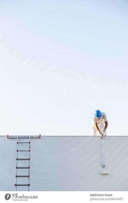 Frontansicht eines jungen Malers, der vom Dach aus malt Mann Farbe Schutzhelm Beruf Individualität Sicherheit bespritzt gefärbt Himmel arbeiten Textfreiraum