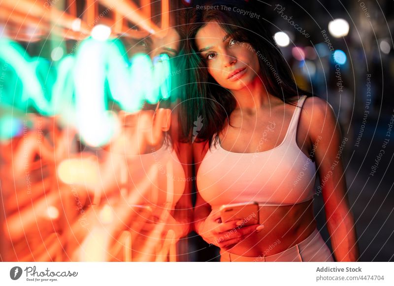 Attraktive Frau surft auf ihrem Smartphone in der Nähe eines beleuchteten Gebäudes glühen leuchten Abend Straße leuchtend Browsen online Textnachricht Internet