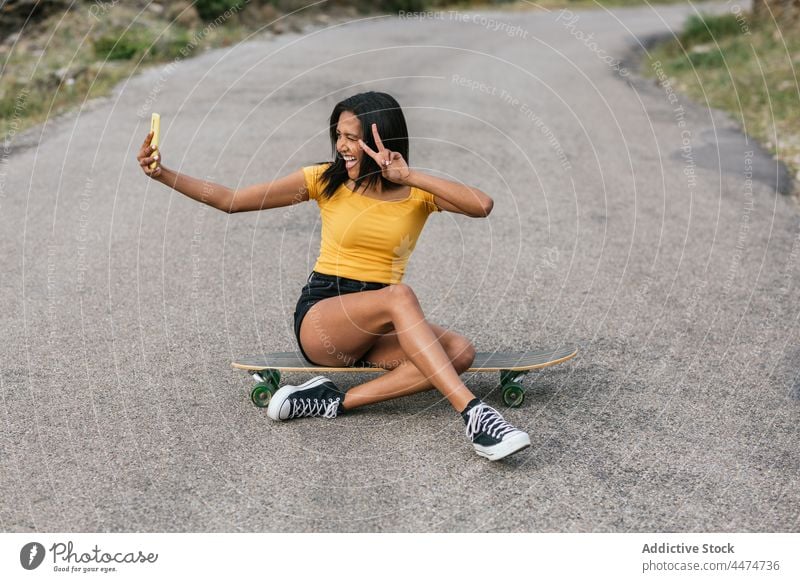 Entzückende ethnische Frau auf Longboard, die ein Selfie mit ihrem Smartphone macht Spaß benutzend Frieden gestikulieren Freude Hobby v-Zeichen zwei Finger Sieg
