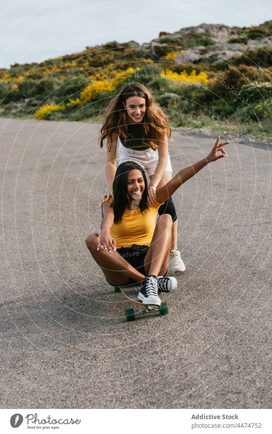 Glückliche Frauen fahren Longboard auf der Straße Freund Mitfahrgelegenheit v-Zeichen Hobby gestikulieren Freundschaft Freizeit bester Freund heiter