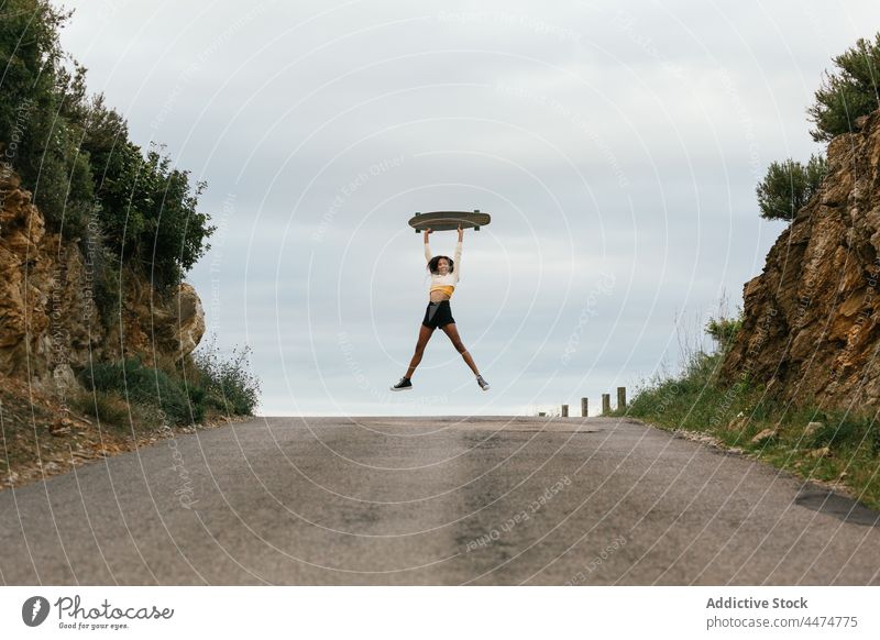 Fröhliche ethnische Frau springt mit Longboard hoch springen Aktivität Energie sich[Akk] bewegen Freude Straße über der Erde Glück aktiv Hobby Bewegung positiv