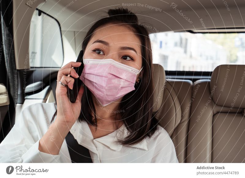 Asiatische Frau, die auf dem Rücksitz eines Taxis mit ihrem Smartphone spricht Passagier Sitz benutzend reden Mundschutz Dienst COVID19 neue Normale Arbeitsweg