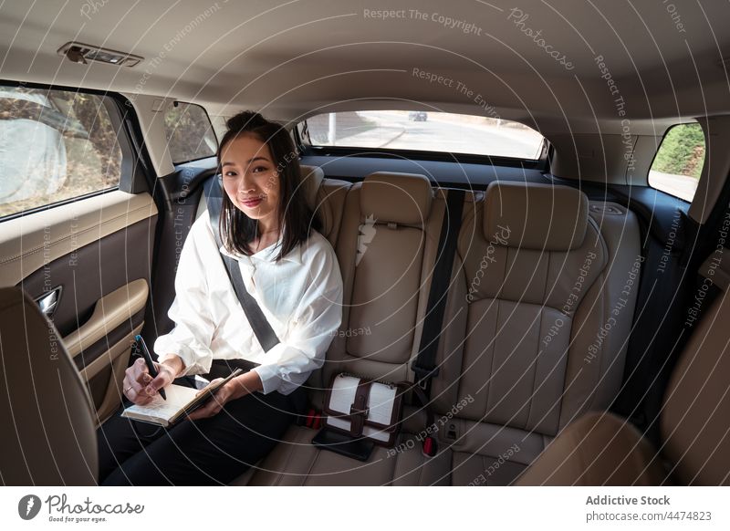 Lächelnde ethnische Frau, die im Taxi Notizen in ein Notizbuch schreibt genießen Passagier Rücksitz Mitfahrgelegenheit Kabine schreiben Notebook Komfort