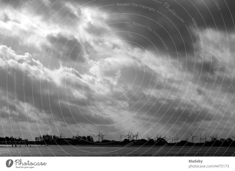 Windräder hinter dem Deich an der Küste der Nordsee in Bensersiel am Wattenmeer mit Wind und Wolken in Ostfriesland in Niedersachsen, fotografiert in neorealistischem Schwarzweiß
