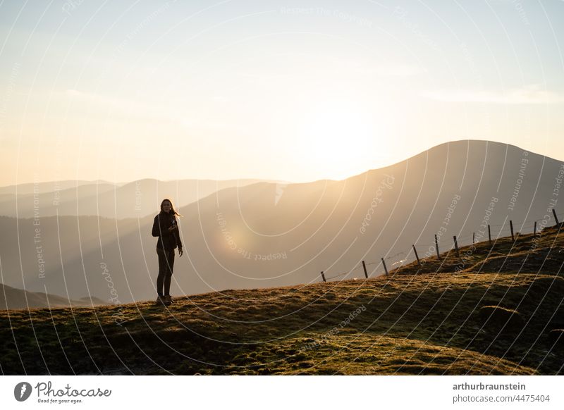 Junge Frau mit langen Haaren und Fotoapparat sucht Motiv bei Sonnenaufgang am Berg berge bergpanorama bewegung draussen fotografie fotografieren freiheit