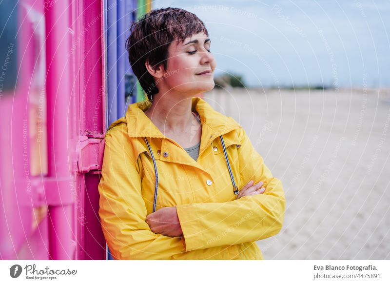 Seitenansicht der entspannten Frau mit geschlossenen Augen tragen gelben Regenmantel über rosa und lila Hintergrund. Bunte Lebensstil im Freien Porträt