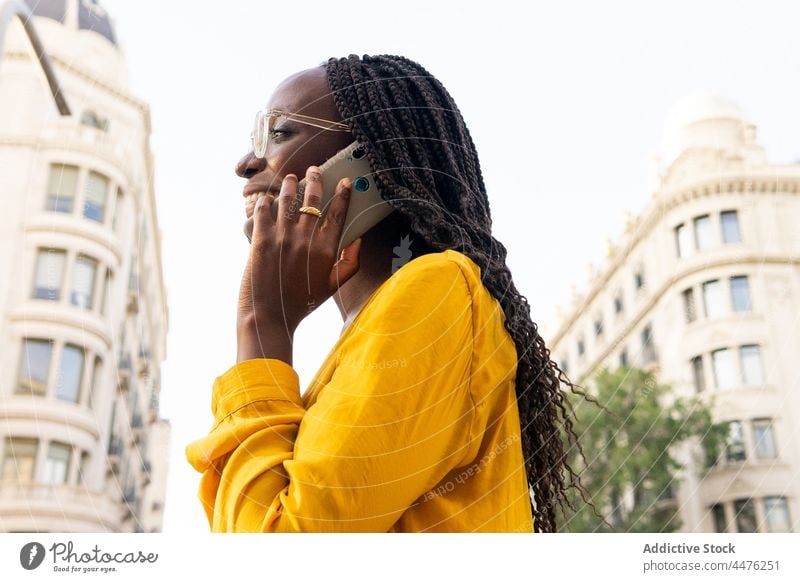 Fröhliche schwarze Frau, die auf der Straße mit ihrem Smartphone spricht Telefonanruf Gespräch diskutieren Großstadt Gebäude Kommunizieren reden Anruf positiv
