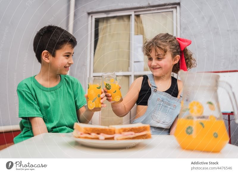 Fröhliche Kinder stoßen mit Saft in der Nähe von Sandwiches an trinken Getränk Klirren Belegtes Brot Lebensmittel Kindheit Snack Appetit & Hunger hungrig Licht