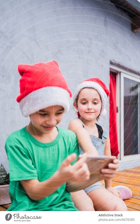 Kinder mit Smartphone und Weihnachtsmannmützen Weihnachten Kindheit Feiertag Weihnachtsmütze Browsen Hobby Surfen Funktelefon Kopfbedeckung festlich farbenfroh