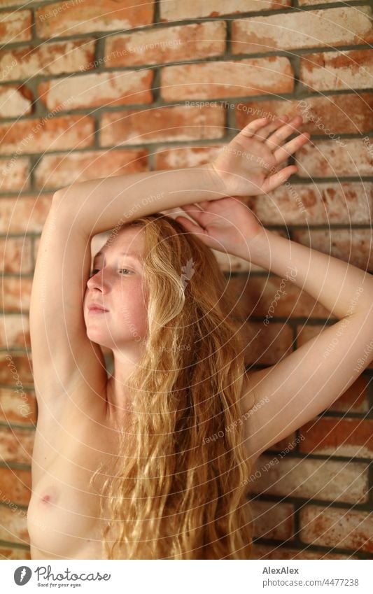 Portrait einer nackten, jungen Frau mit Sommersprossen und roten Haaren, die in einer Tanzpose vor einer Backsteinwand verharrt Porträt nah Nähe Ausstrahlung