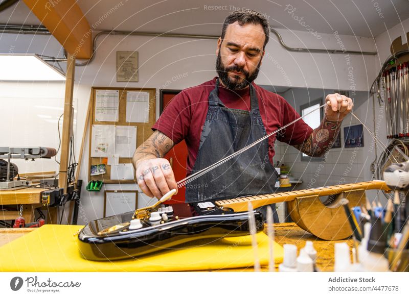 Konzentrierter Mann wechselt in der Werkstatt die Saiten einer Gitarre Instrument Fähigkeit Handwerk Schnur Gerät Meister Kunsthandwerker männlich professionell