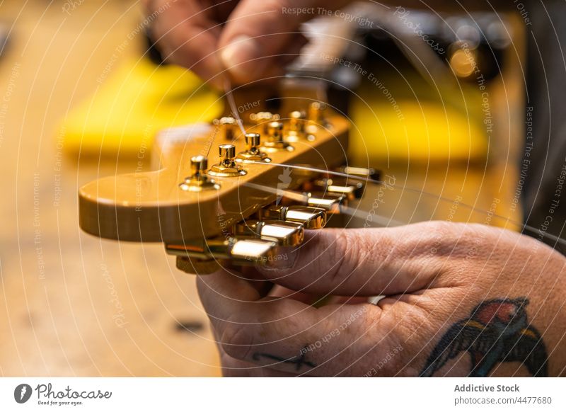 Professioneller Handwerker beim Aufziehen der Saiten auf die Gitarre Mann Kunsthandwerker Musiker Schnur Instrument Gitarrenspieler Werkstatt Gerät installieren