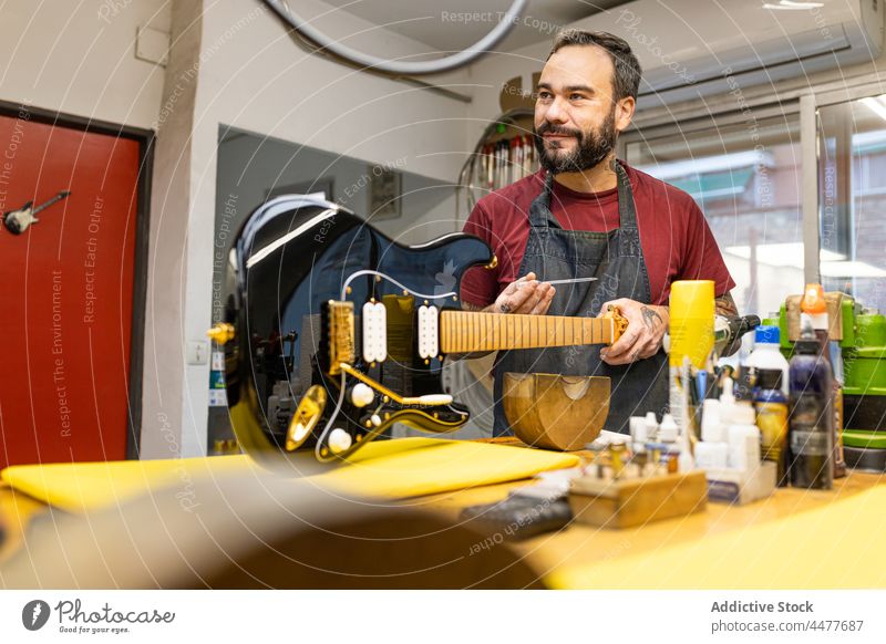 Positiver Mann, der eine E-Gitarre im Studio repariert Instrument Fähigkeit elektrisch Reparatur Gerät Basteln Kunsthandwerker professionell männlich Werkstatt
