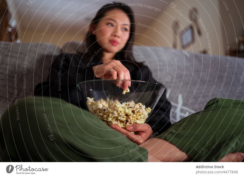Junge asiatische Frau sitzt auf dem Sofa und isst Popcorn essen Popkorn Liege Beine gekreuzt sitzen zu Hause sich[Akk] entspannen genießen Windstille Freizeit
