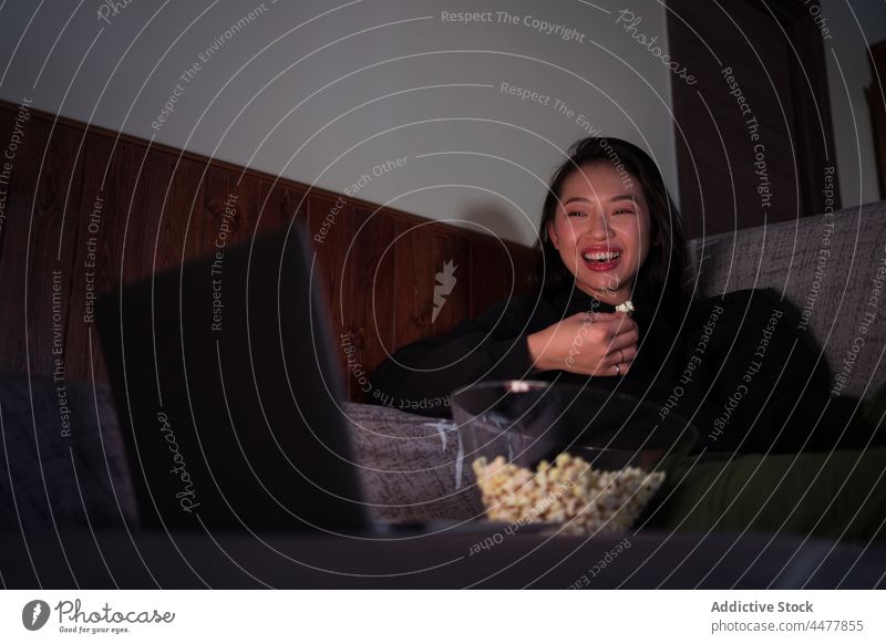 Junge asiatische Frau sitzt auf dem Sofa und isst Popcorn essen Laptop Popkorn Liege Computer sitzen zu Hause sich[Akk] entspannen genießen Windstille Freizeit