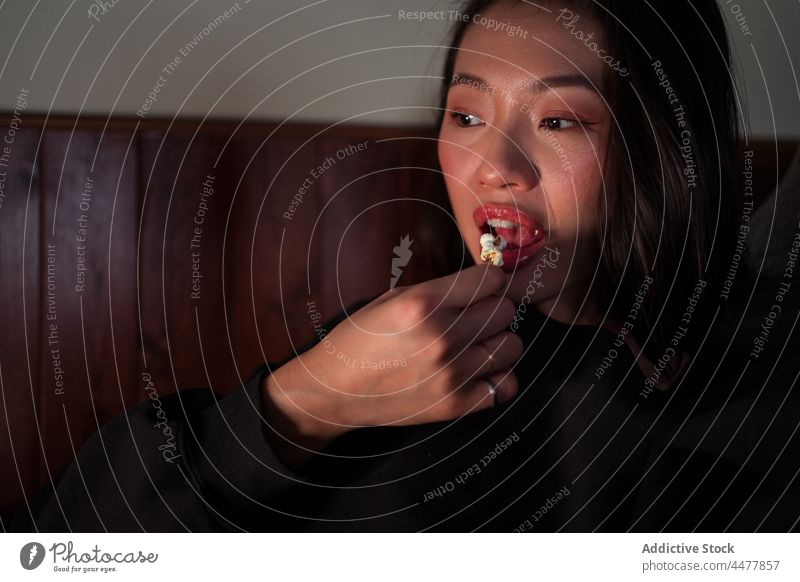 Junge asiatische Frau sitzt auf dem Sofa und isst Popcorn essen Popkorn Liege sitzen zu Hause sich[Akk] entspannen genießen ethnisch Windstille Freizeit