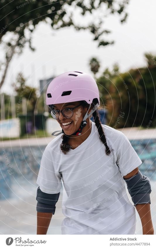 Fröhliche afroamerikanische Frau mit rosa Helm und Ellbogenschützern Schlittschuh Skateplatz Schutzhelm Generation Lächeln Freiheit behüten Spaß Ellbogenpolster