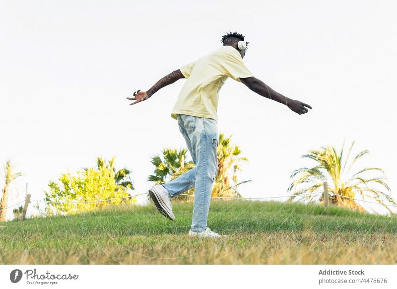 Anonymer schwarzer Mann mit Kopfhörern zwischen Palmen stehend Tanzen Park lässig Musik Sonne Freizeit Kälte Stil ruhen zuhören Sonnenlicht Windstille Freiheit