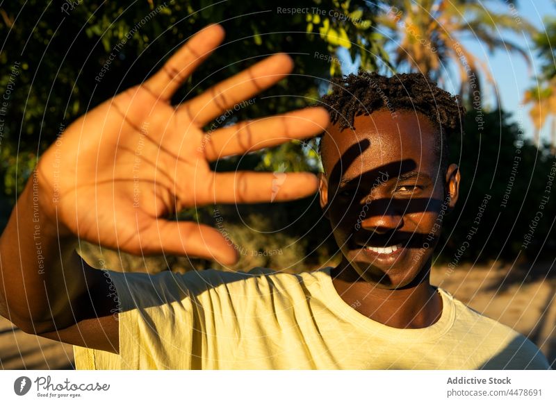 Schwarzer Mann mit schelmischem Lächeln schaut in die Kamera Deckblatt positiv freundlich Sonnenuntergang heiter gestikulieren Sonnenlicht Menschliches Gesicht