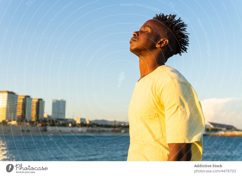 Schwarzer Mann mit geschlossenen Augen auf der Straße Himmel Sonnenuntergang Windstille Gebäude Abend friedlich Outfit Großstadt männlich Afroamerikaner schwarz