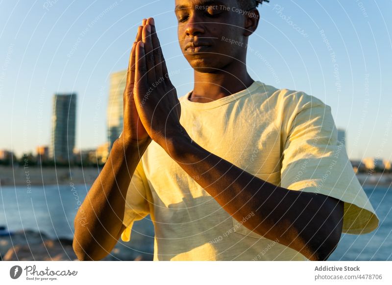 Schwarzer Mann mit geschlossenen Augen auf der Straße Himmel Namaste Sonnenuntergang gestikulieren Hände Windstille Gebäude Abend friedlich Outfit Großstadt