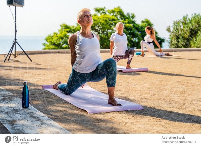 Frauen, die einen halbmondförmigen Ausfallschritt auf dem Knie mit verschränkten Händen während einer Yoga-Sitzung machen üben Park Sportkleidung Wellness