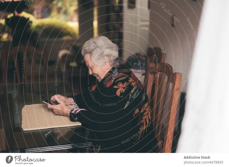 Ältere Frau mit Gerät sitzt am Tisch Tablette zu Hause Tee Apparatur Rentnerin Senior älter gealtert trinken Browsen benutzend Tasse Lächeln warm