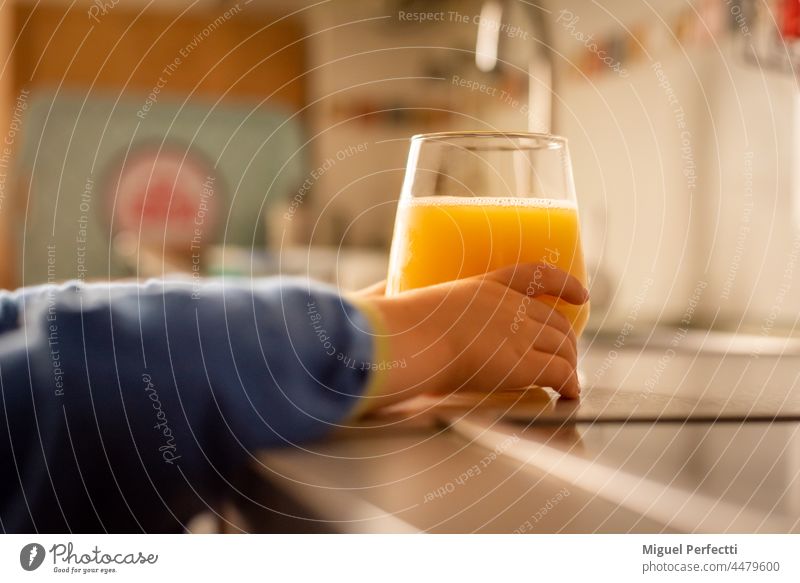 Kinderhände, die nach einem Kristallglas mit Orangensaft auf dem Küchentisch greifen. Saft orange Hände Glas trinken Frühstück Getränk Vitamin Frucht