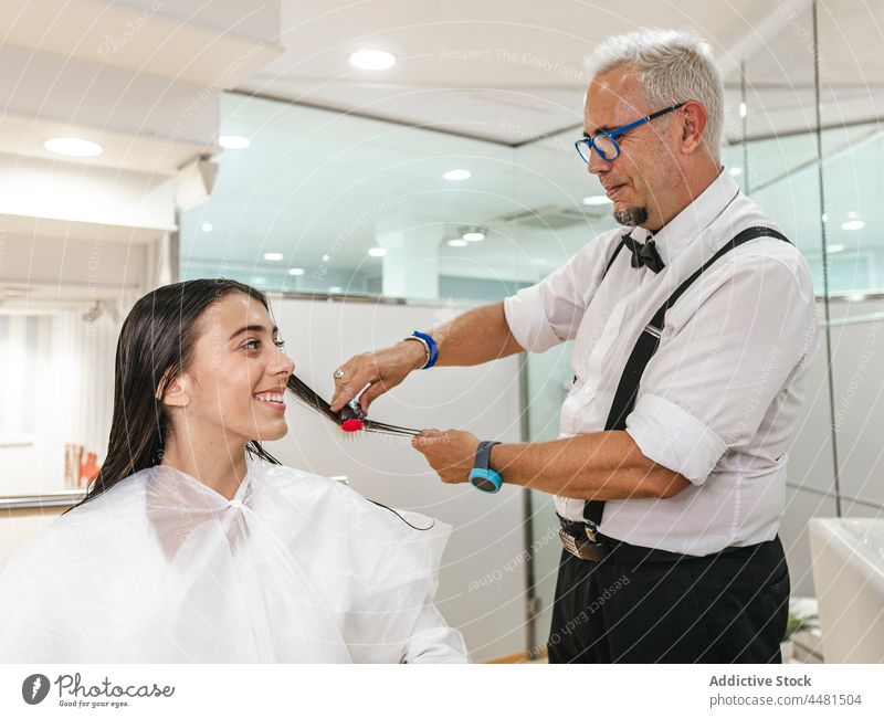 Männlicher Friseur bei der Arbeit mit dem Haar eines Kunden Mann Frau Meister Klient Kamm Salon Frisur heiter Kap professionell Stil Prozess Lächeln Job Beruf