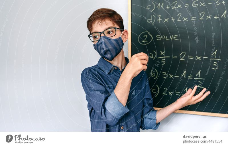 Junge mit Maske löst Matheaufgaben an der Tafel Gesichtsmaske Schule Coronavirus Matheunterricht neue Normale Lösung zu erklären. Gleichungen Sicherheit Virus